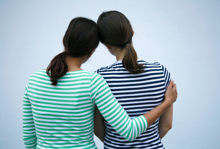 Two women seen from behind with arms around each other.