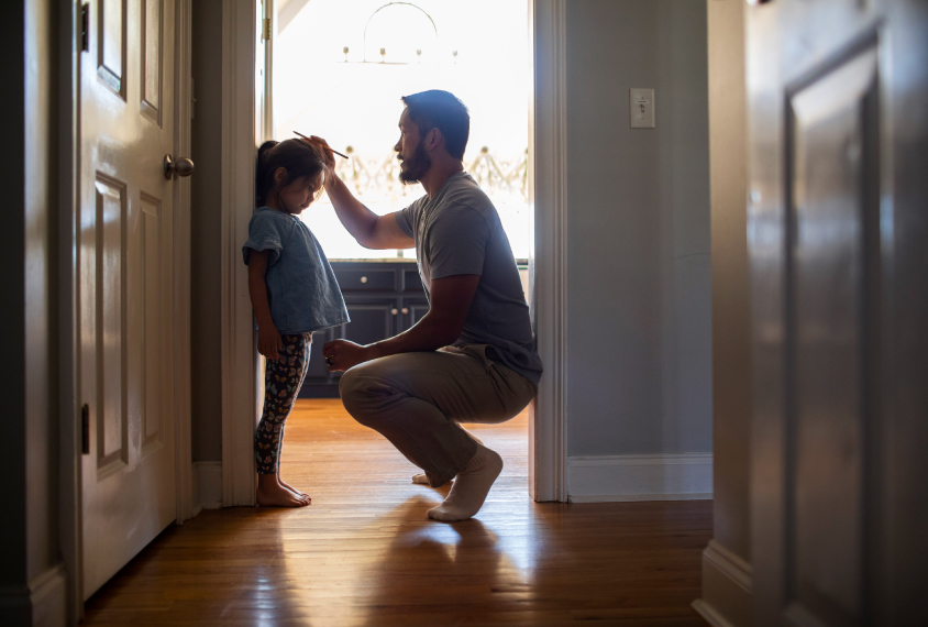 Photograph of a father measuring his daughter’s height against a doorway.