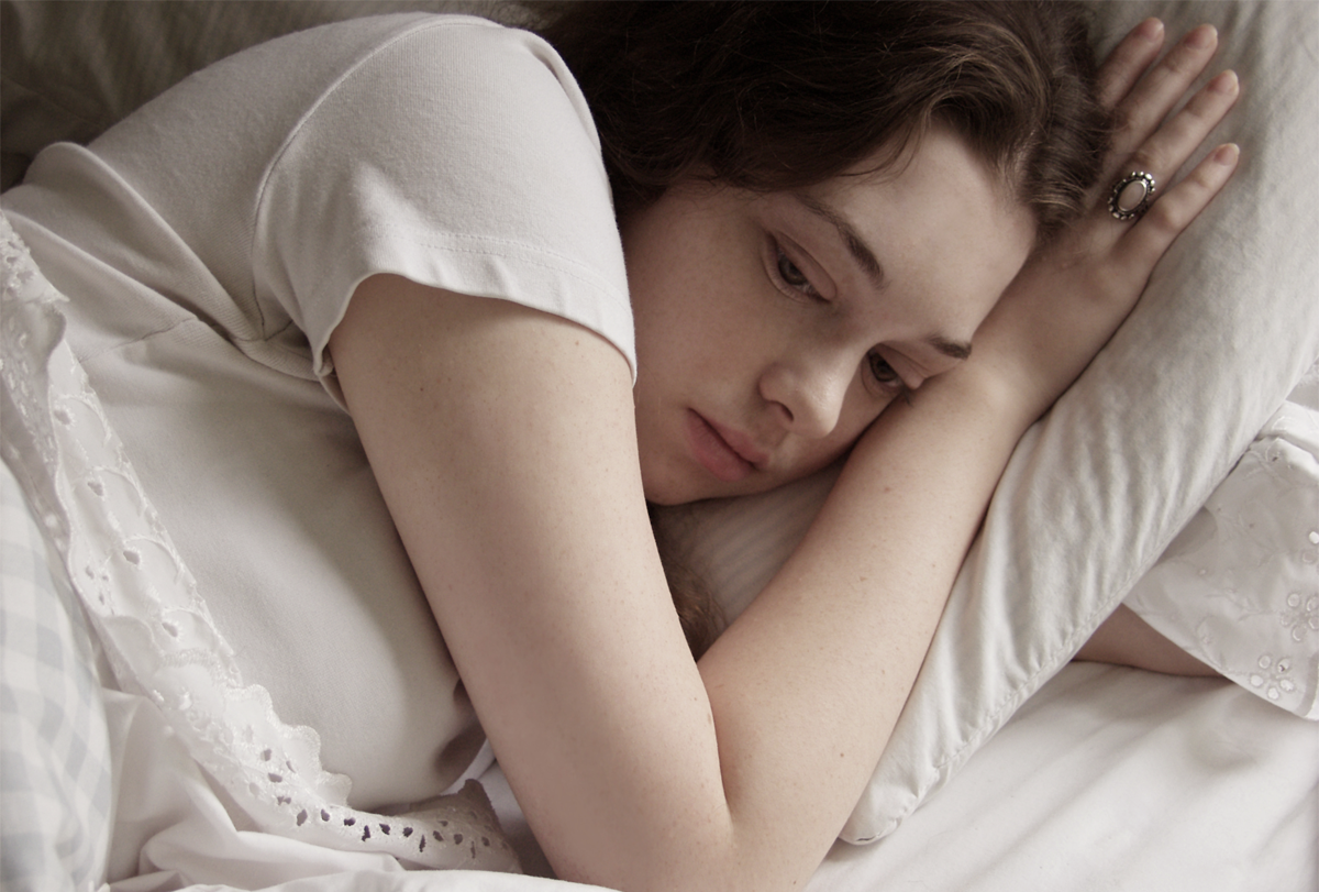 Photograph of a young girl laying in bed with her eyes open.