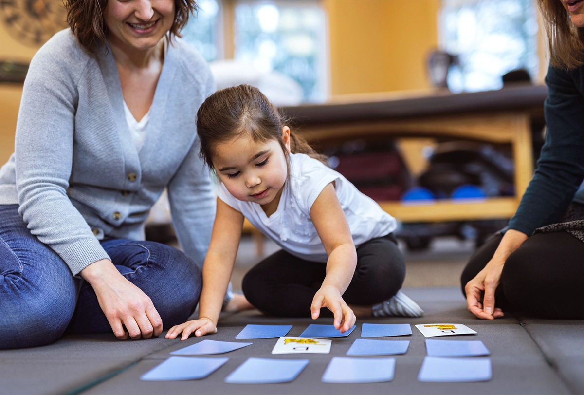 Preschool-age girl plays matching card game with mother and therapist.