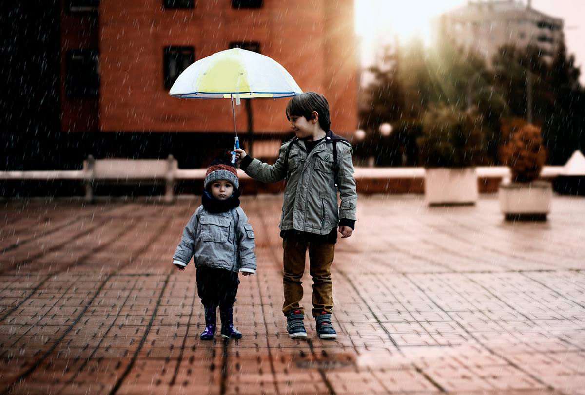 A child holds an umbrella over another, smaller child.