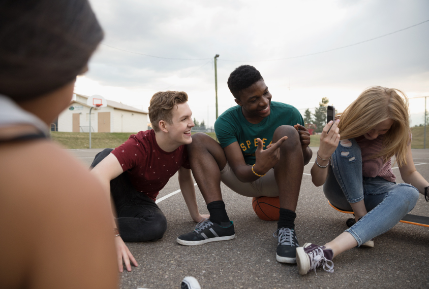 four teenage friends sitting outside in parking lot