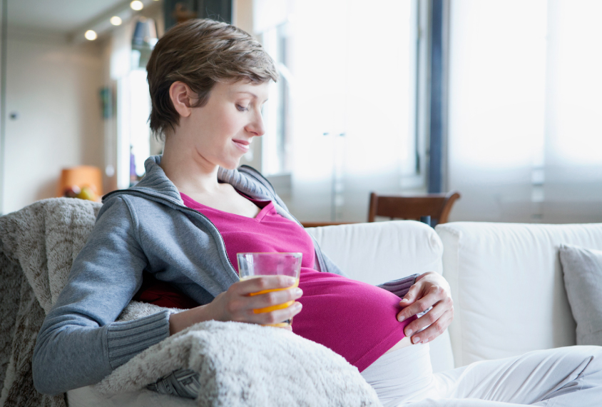 pregnant mother sitting with a glass of water touching belly