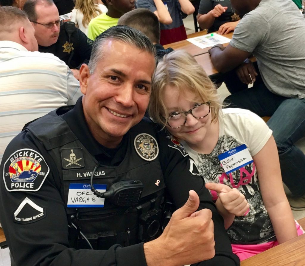 A smiling police officer poses with a child, also smiling.