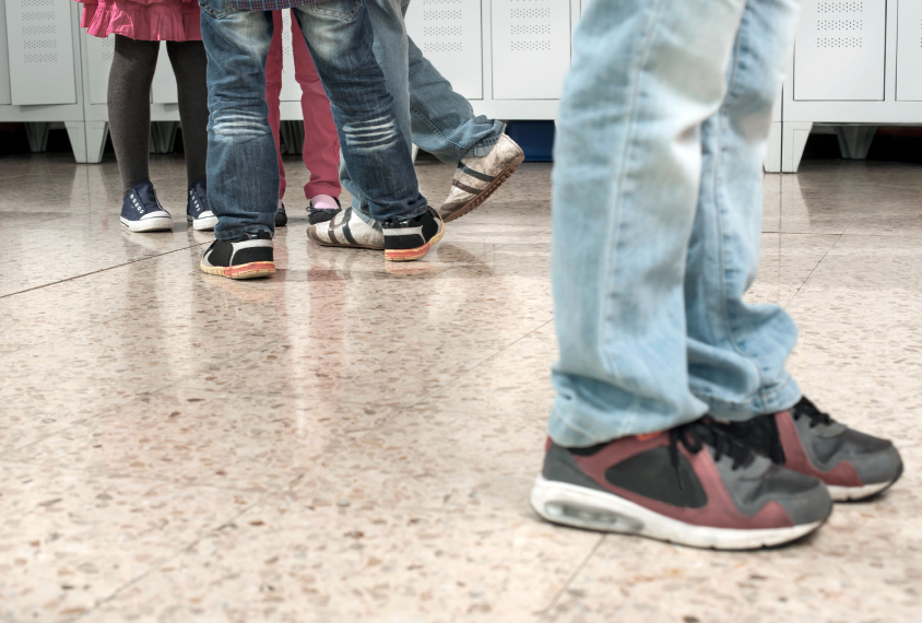 Kids shoes in hallway showing one boy standing alone by a group.