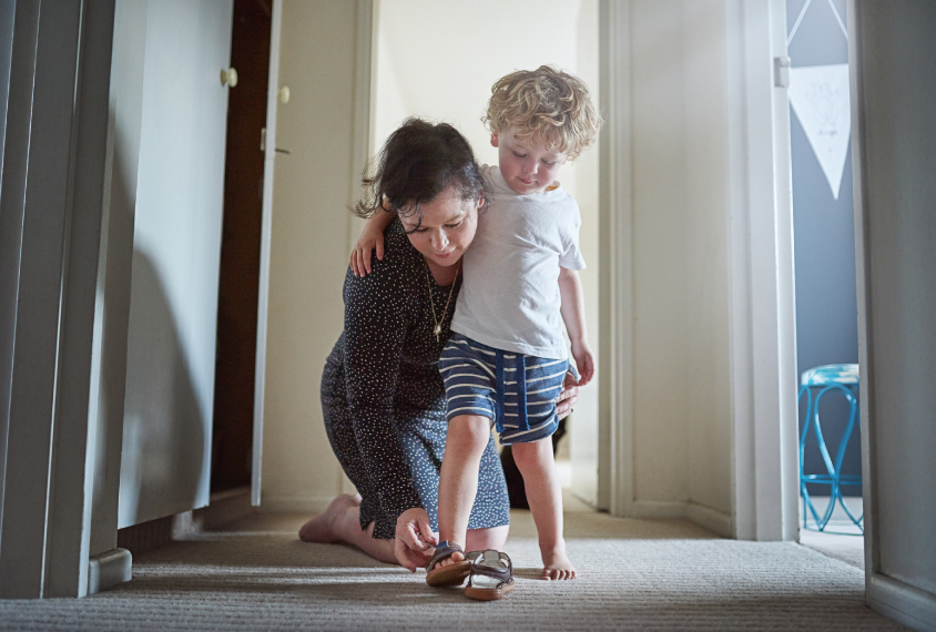 A woman helps her son put on his shoe.