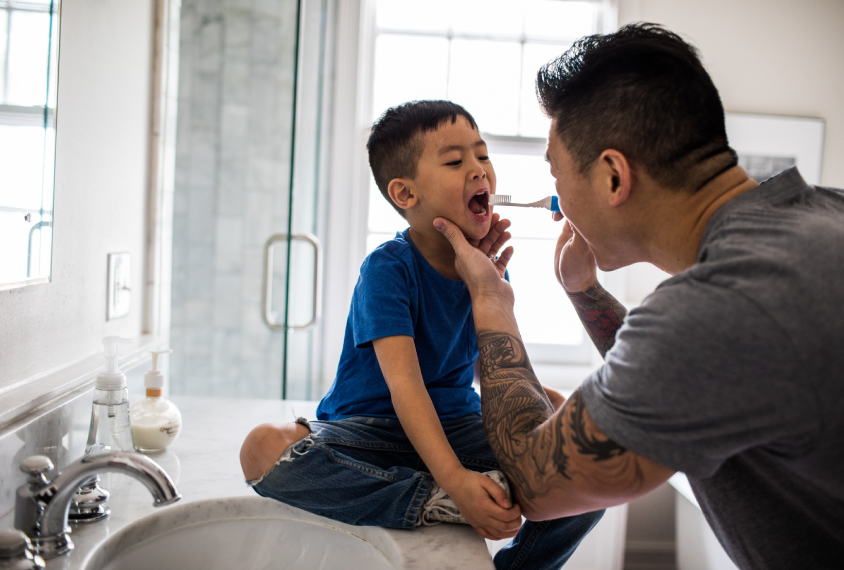 Father helping boy brush teeth