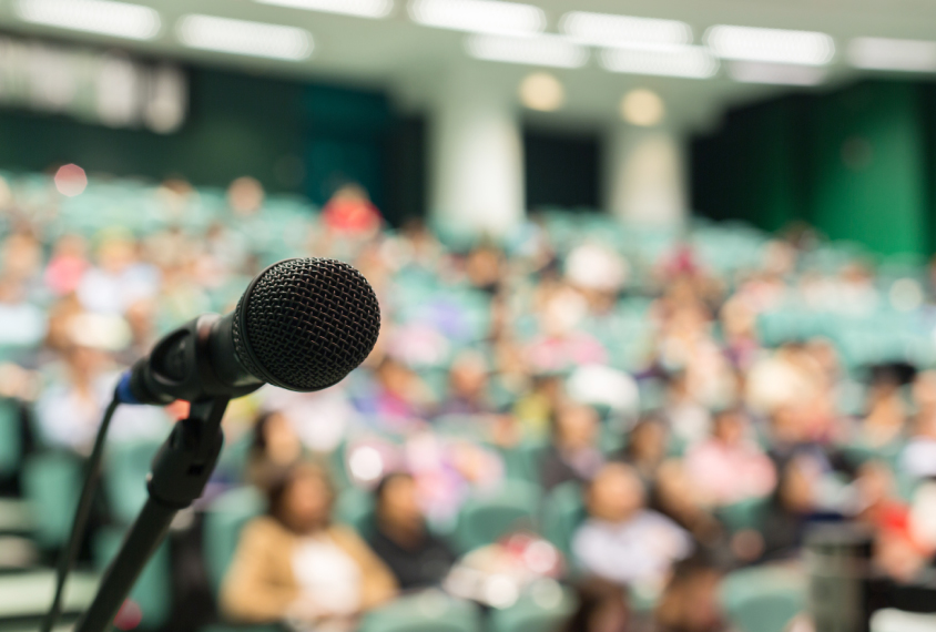 Auditorium conference scene with microphone in foreground.