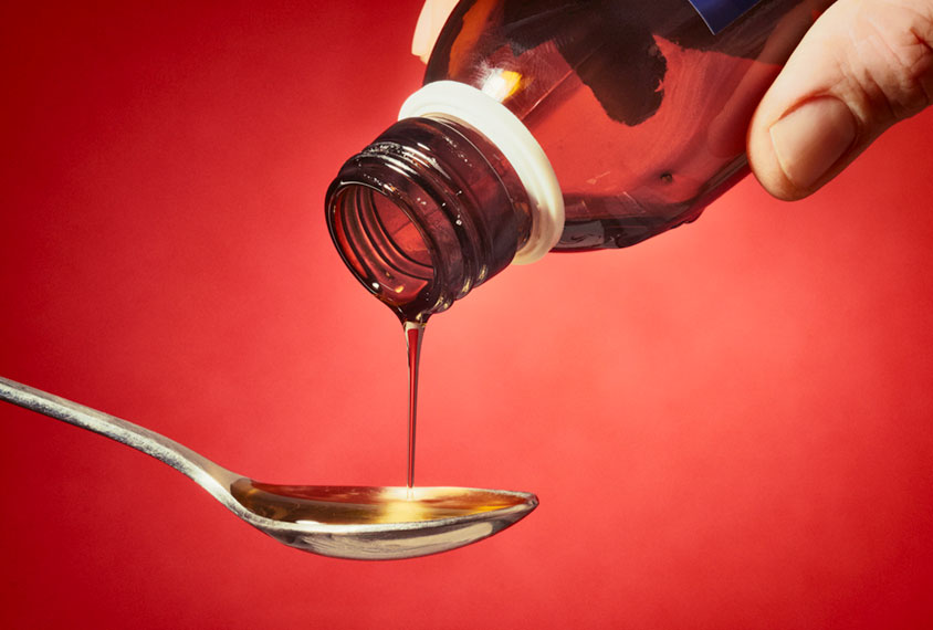 Liquid medicine being poured from bottle onto spoon.