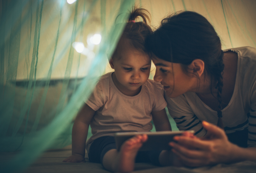 Parent reads to her child at night in a makeshift text with cozy lights.
