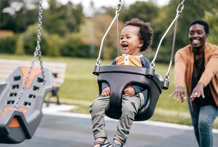 Black mother pushing her child on swing at playground.