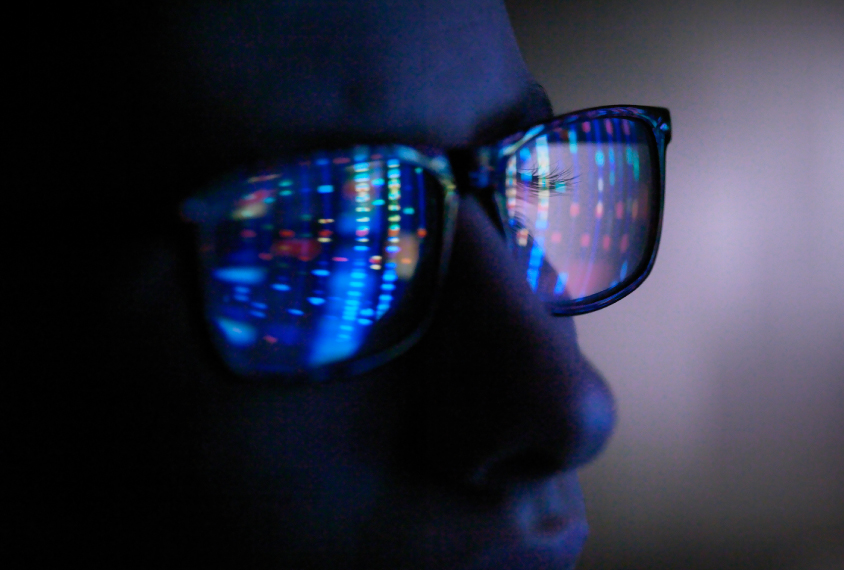 Computer screen reflection in spectacles of DNA profile, close up of face