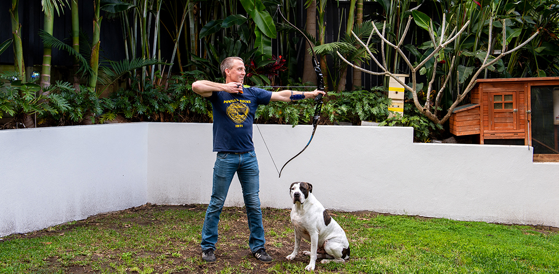 Scientist Ethan Scott takes aim with a bow and arrow in his backyard.