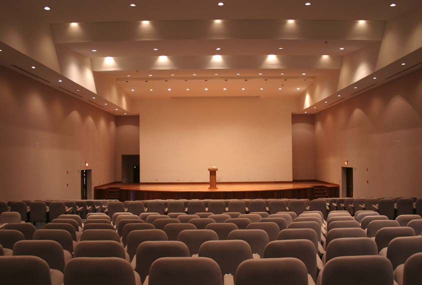 Photo of empty conference room with empty stage and podium in distance.