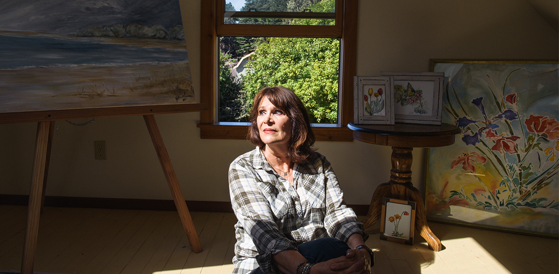 Portrait of Judy Van De Water at her home in Fort Bragg, CA, with her paintings.