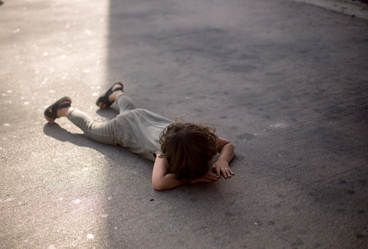 Photograph of a young child lying face-down on pavement in apparent frustration.