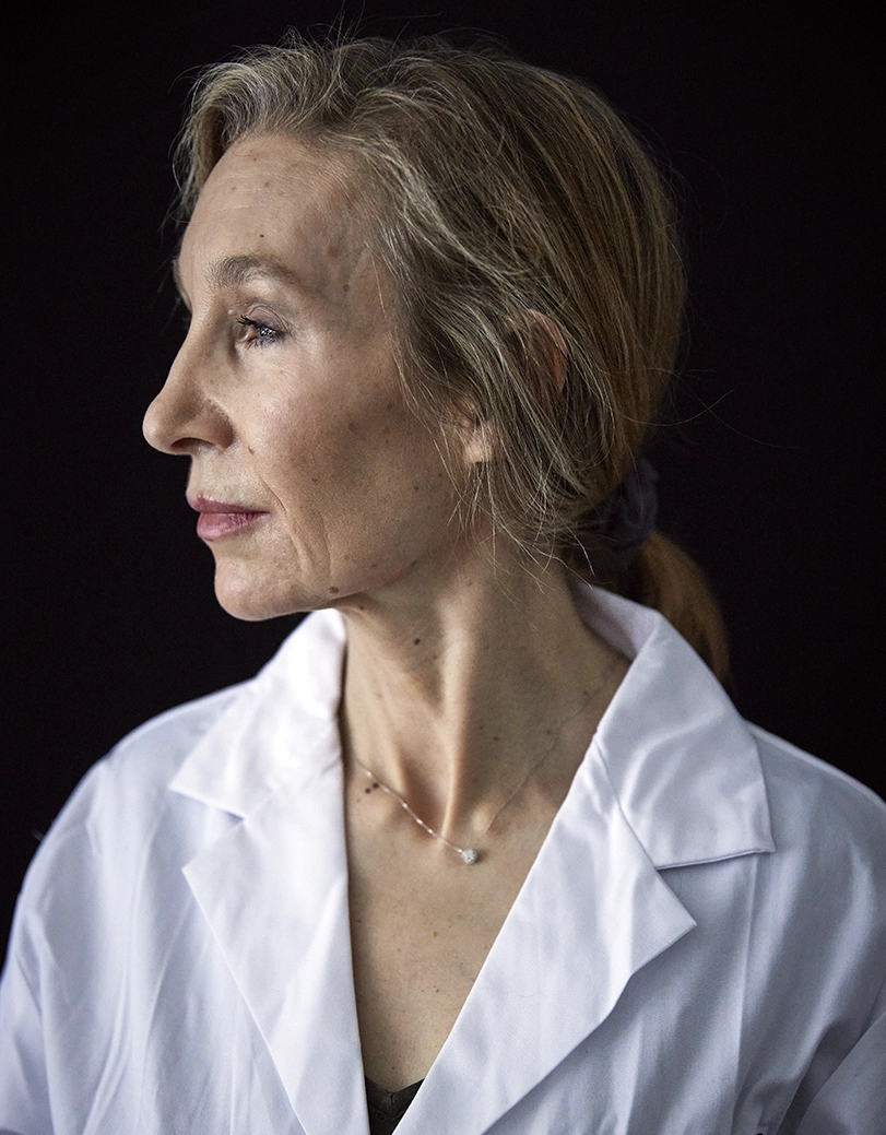 Portrait of scientist Sheena Josselyn in her lab coat, seen in profile on a dark backgound.