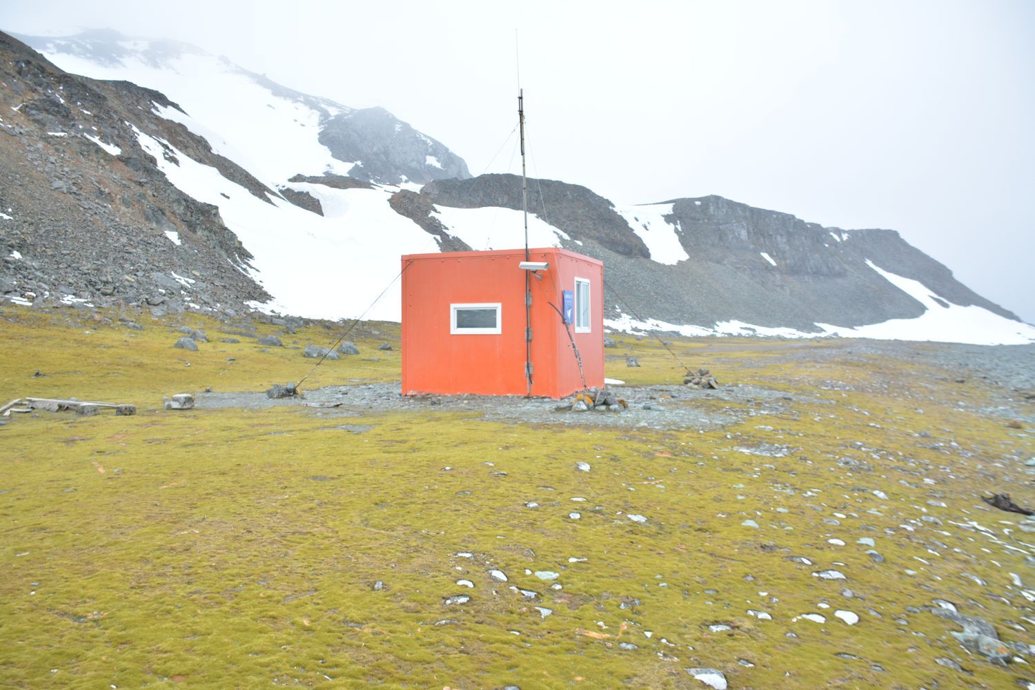 Photograph of a small, orange, cubic building in Antarctica.