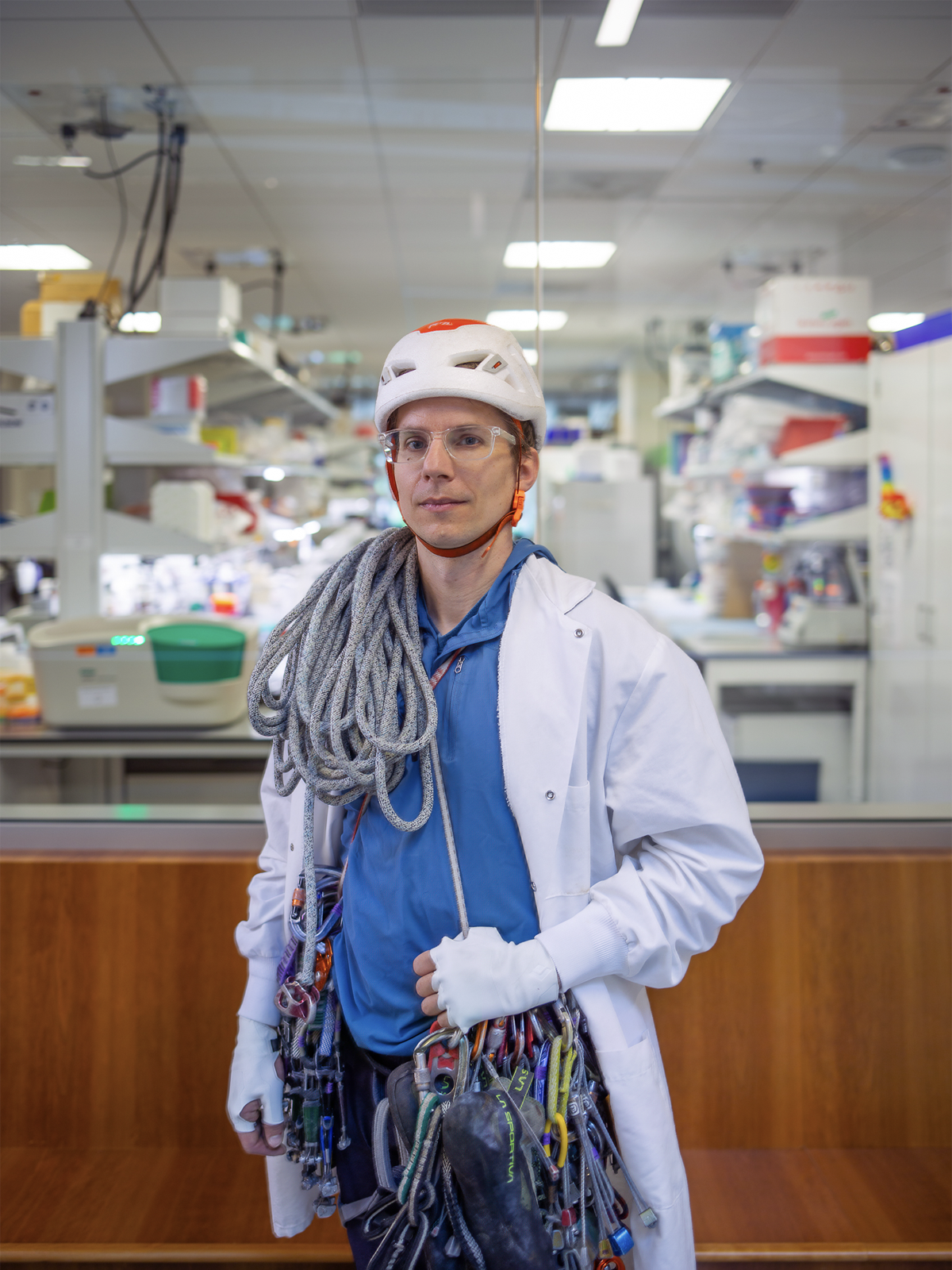 Portrait of Kaspar Podgorski standing in his lab wearing a helmet with a climbing rope over his shoulder.