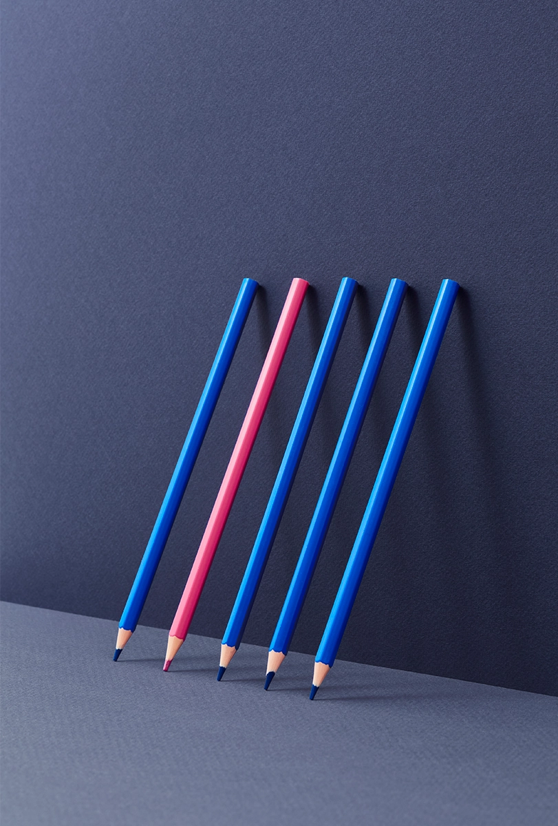 Photograph of a pink pencil standing out from a row of blue pencils.