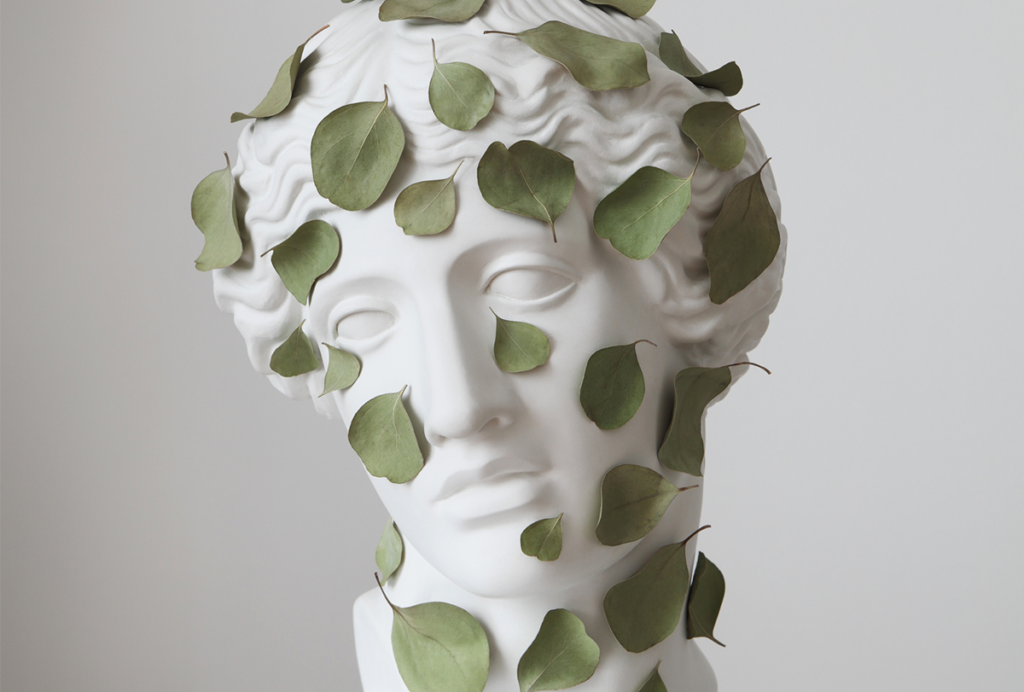 A marble bust of a face that is covered in real leaves.