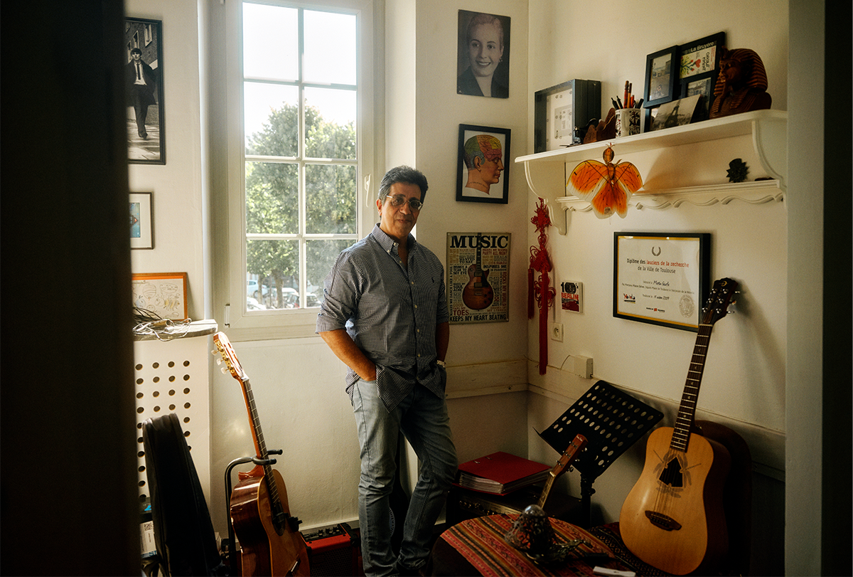 Martin Giurfa stands in a room with several acoustic guitars.