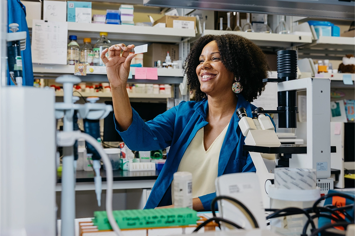 Photograph of Theanne Griffith holding up a microscope slide in her lab.