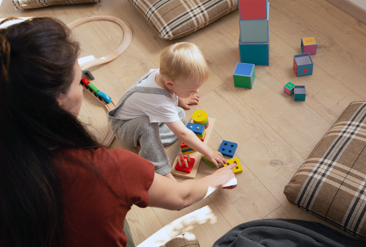 Photograph of a child sitting on the floor playing with blocks while an adult watches.