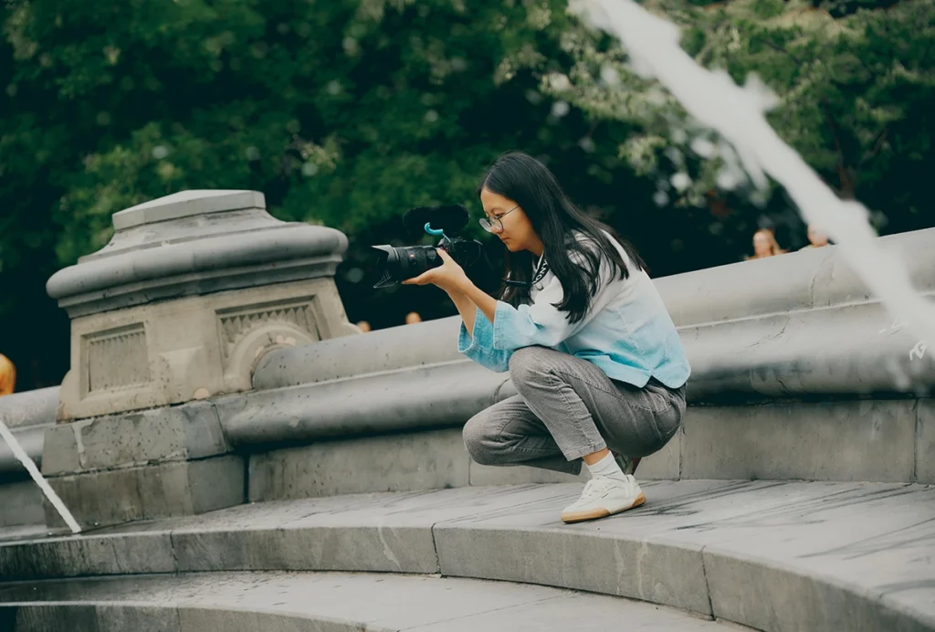 Photograph of Pei Yuan Zhang squatting and looking through the lens of a camera.