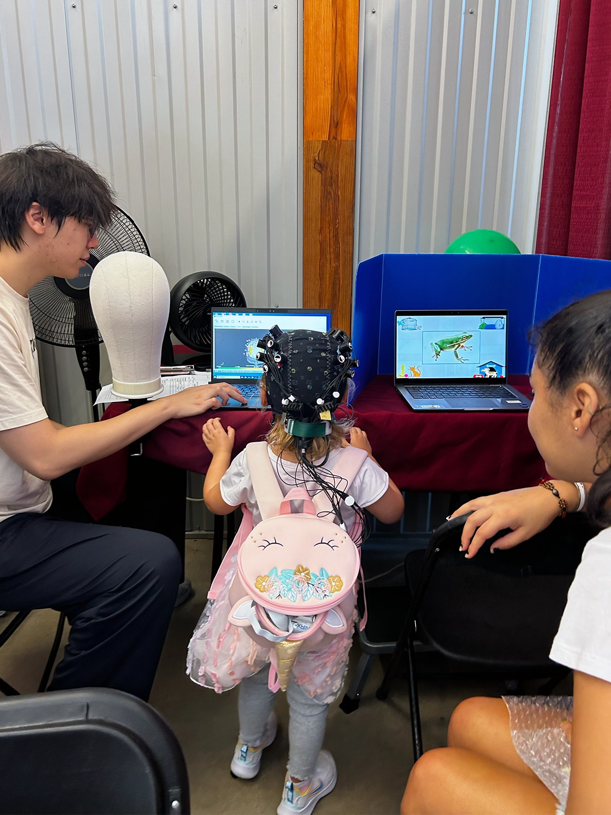 Photograph of a child standing in front of a laptop and performing a cognitive test.