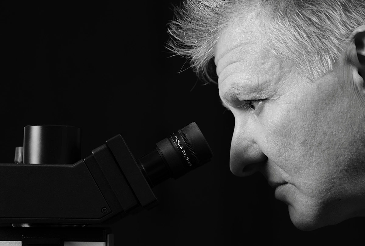 Close-up, black-and-white photograph of Bryan Jones looking into a microscope.