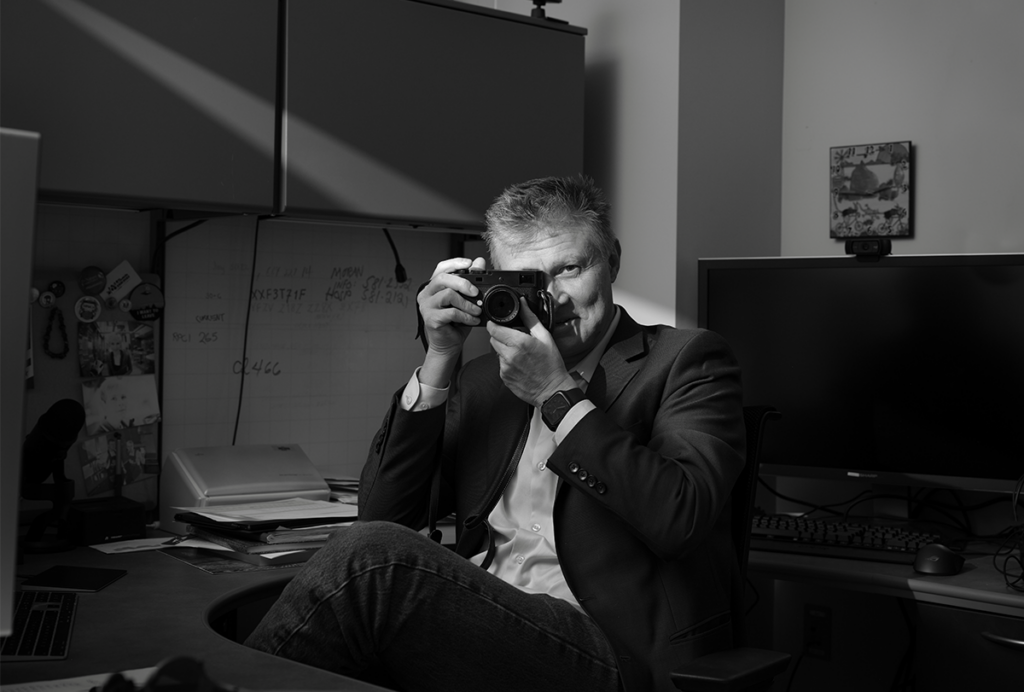 Black-and-white photograph of Bryan W Jones holding a camera and pointing it back at the photographer.