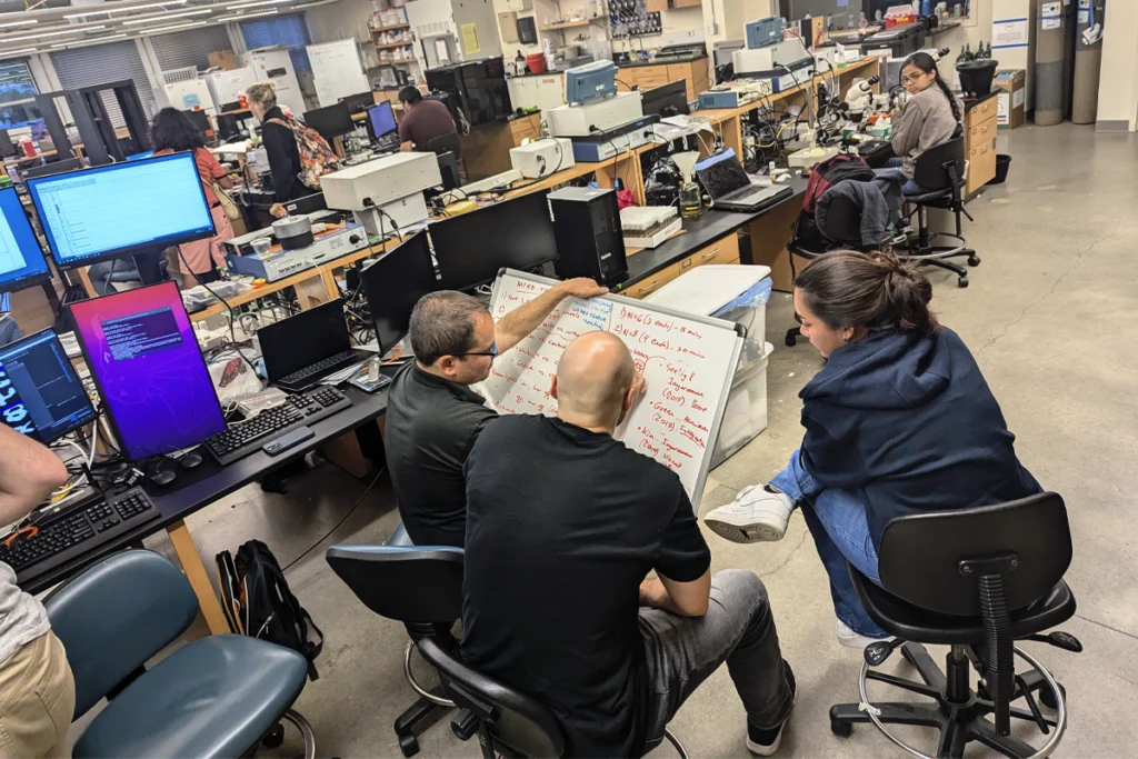 Multiple people look together at a whiteboard in a lab.