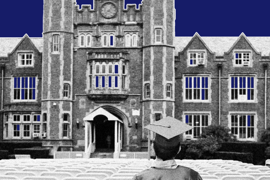 A student in a cap and gown sits alone in a row of folding chairs in front of a large brick building.